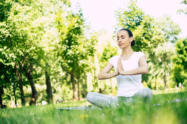 Yoga féminin au parc. Jeune femme brune en posture de lotus assis sur l'herbe verte dans le parc. Concept de calme et de méditation