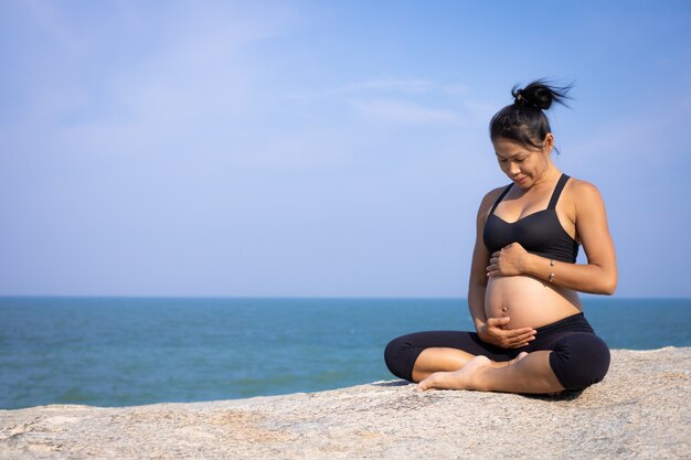 Yoga femme asiatique enceinte sur l'heure d'été coucher de soleil sur la plage