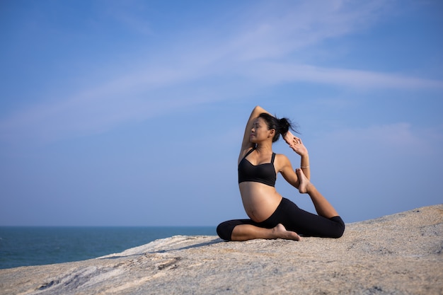 Yoga femme asiatique enceinte sur l'heure d'été coucher de soleil sur la plage