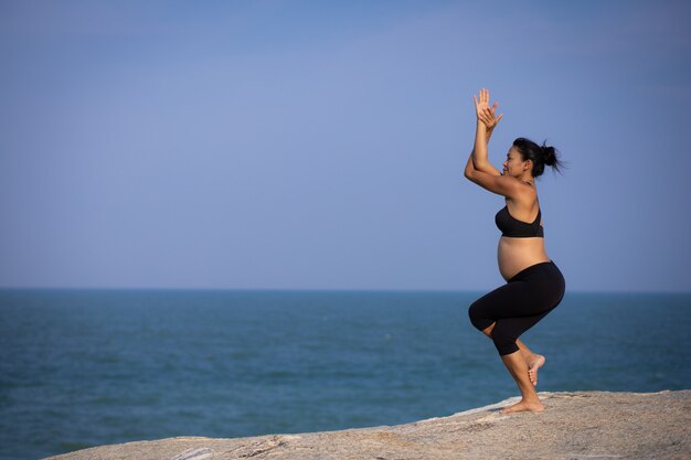 Yoga femme asiatique enceinte sur l'heure d'été coucher de soleil sur la plage