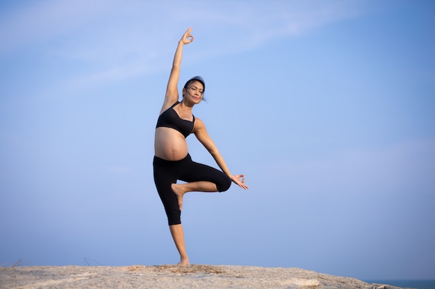Yoga femme asiatique enceinte sur l'heure d'été coucher de soleil sur la plage