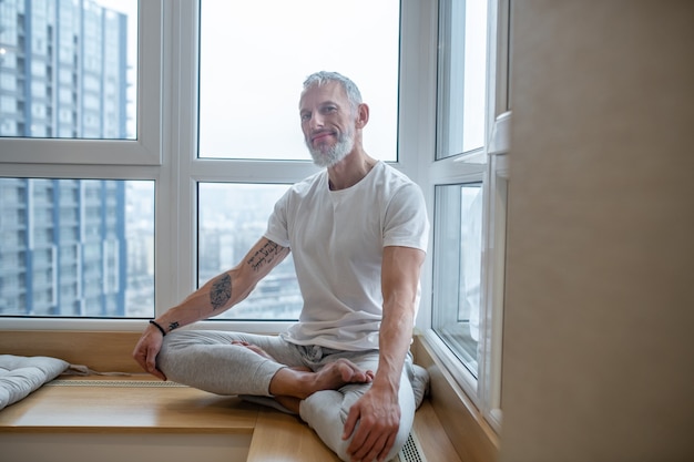 Yoga. Un homme mûr dans un t-shirt blanc faisant du yoga et ayant l'air concentré