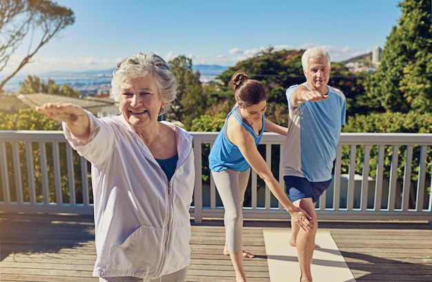 Le yoga les maintient en forme et en bonne santé Photo d'un couple de personnes âgées faisant du yoga avec un instructeur sur leur terrasse à l'extérieur