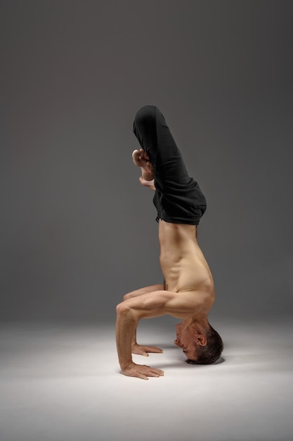 Yoga masculin debout sur la tête et les mains, méditation, mur gris Homme fort faisant de l'exercice yogi, formation asana, concentration maximale