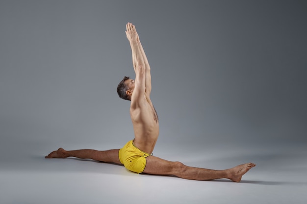 Yoga masculin est assis sur une ficelle, position de relaxation, fond gris. Homme fort faisant de l'exercice yogi, entraînement asana, concentration maximale, mode de vie sain