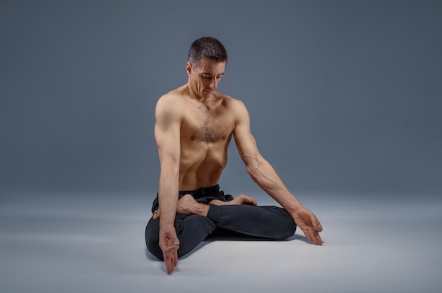 Yoga masculin madite en pose classique, position de méditation, fond gris. Homme fort faisant de l'exercice yogi, entraînement asana, concentration maximale, mode de vie sain