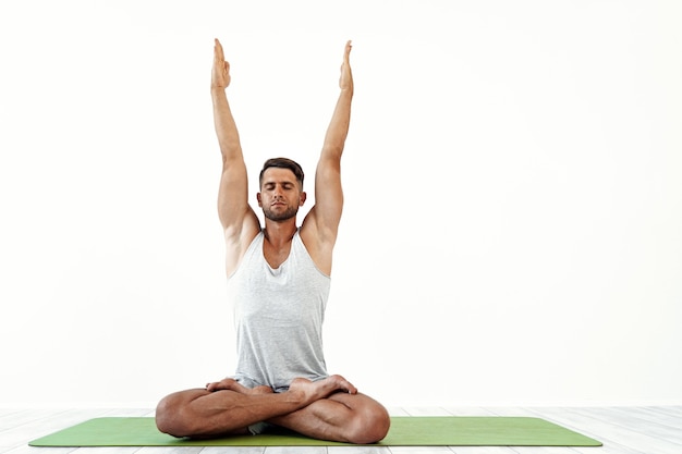 Yoga masculin médite dans une pose classique en studio sur blanc