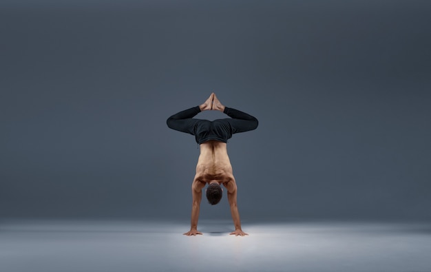 Le yoga masculin se partage sur les mains, vue arrière, mur gris Homme fort faisant de l'exercice yogi, formation asana, concentration maximale, mode de vie sain