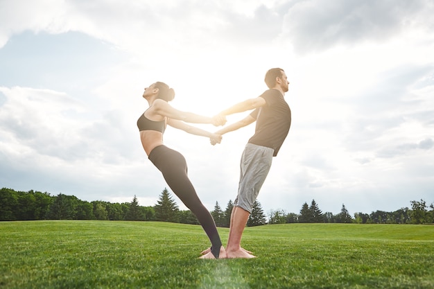 Yoga en paire beau jeune couple pratiquant le yoga acro ensemble et s'étirant dans la nature sur