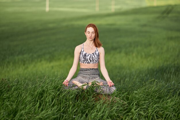 Yoga en plein air. Femme heureuse, faire des exercices de yoga, méditer dans un parc ensoleillé. Concept de mode de vie sain et de détente. Jolie femme pratiquant le yoga sur l'herbe