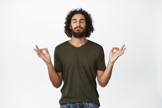 Yoga et pleine conscience Jeune homme détendu respirant calmement méditant en écoutant un podcast debout sur fond blanc