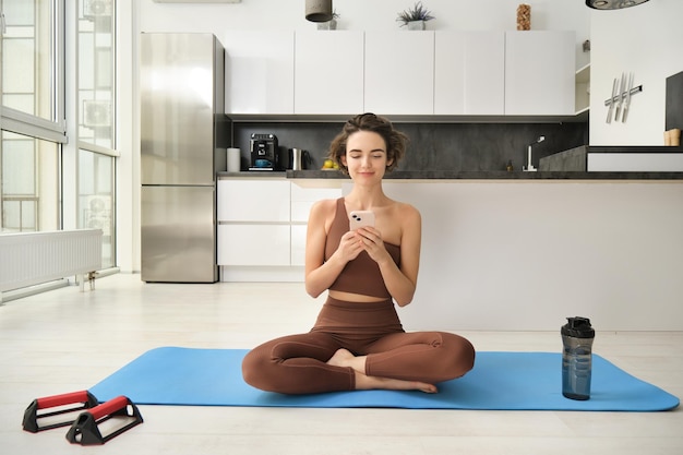 Yoga et sport à la maison concept jeune femme assise à rome lumineuse avec téléphone portable faisant de l'exercice sur