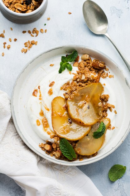 Yogourt grec avec poire caramélisée, granola, noix et sucre fondu pour un petit-déjeuner sain sur une assiette en céramique grise