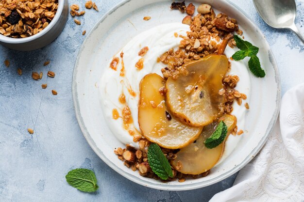 Yogourt grec avec poire caramélisée, granola, noix et sucre fondu pour un petit-déjeuner sain sur une assiette en céramique grise