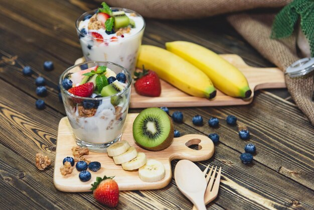 Photo yogourt grec sain avec granola et baies mixtes sur table en bois et beaucoup de fruits concept de nourriture et de dessert