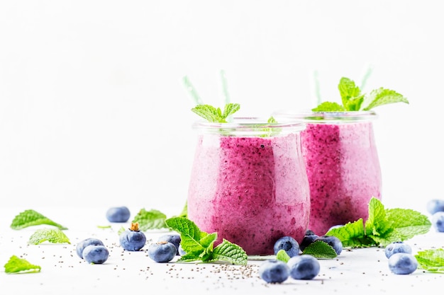 Yogourt maison violet ou smoothie aux myrtilles graines de chia et feuilles de menthe dans des bocaux en verre sur fond gris mise au point sélective