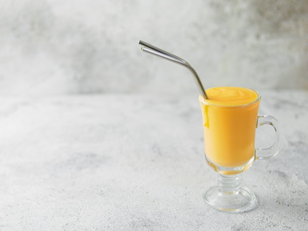 Yogourt à la mangue jaune ou smoothie sur fond de ciment gris avec espace de copie à gauche Turmeric Lassie ou lassi en verre avec pailles métalliques