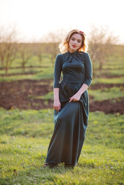 Yong élégante fille blonde à la robe verte sur le jardin au printemps sur coucher de soleil.