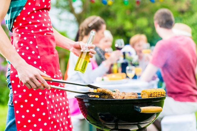 Yong man au barbecue en tournant la viande, en arrière-plan des amis organisent une garden-party