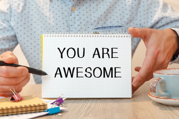 YOU ARE AWESOME est écrit sur un bloc-notes sur un bureau avec des accessoires de bureau.