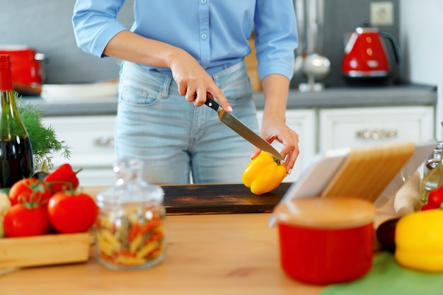 Young blonde caucasian woman couper des légumes pour la salade dans sa cuisine