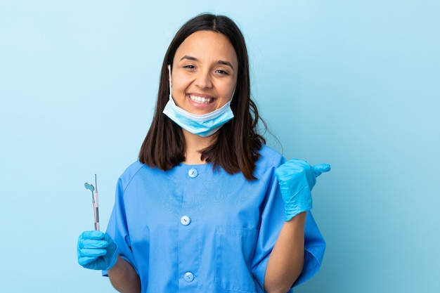 Young brunette mixed race dentist woman holding tools sur mur isolé avec les pouces vers le haut de geste et souriant