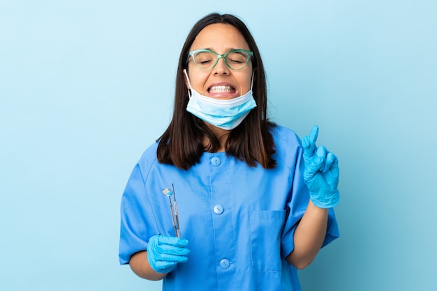 Young brunette mixed race dentist woman holding tools over isolé avec les doigts traversant et souhaitant le meilleur