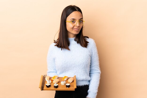 Young brunette mixed race woman holding sushi sur fond isolé ayant des doutes