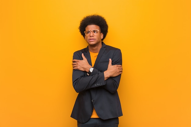 Young business african american man sur un mur orange va froid en raison de la basse température