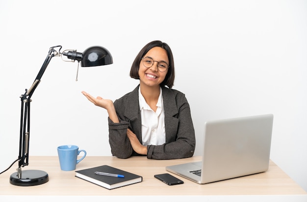 Young business mixed race woman working at office holding copyspace imaginaire sur la paume pour insérer une annonce