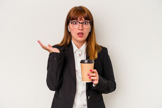 Young caucasian business curvy woman holding a coffee isolé sur fond blanc surpris et choqué.