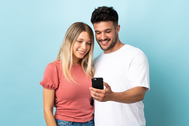 Young caucasian couple on blue envoi d'un message ou d'un e-mail avec le mobile