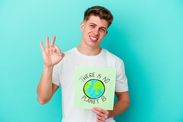 Young caucasian man holding a il n'y a pas de plaque-étiquette planète b isolé sur mur bleu