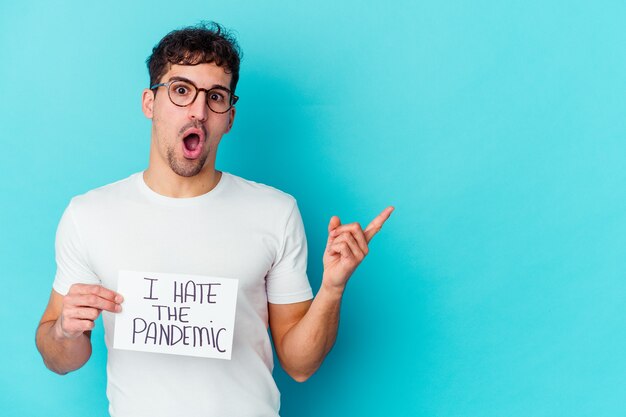 Young caucasian man holding a je déteste la pancarte pandémique isolée pointant vers le côté