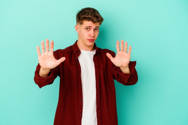 Young caucasian man isolated on blue wall étant choqué en raison d'un danger imminent