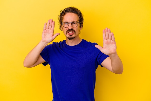 Young caucasian man isolated on yellow wall étant choqué en raison d'un danger imminent