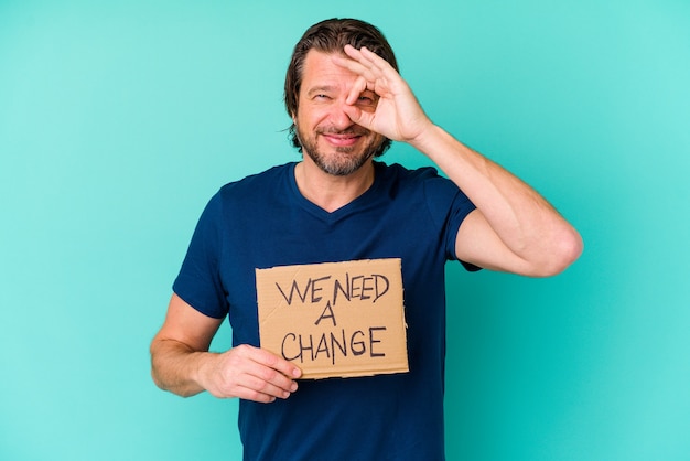 Young caucasian middle age man holding a Nous avons besoin d'une pancarte de changement isolé sur fond bleu