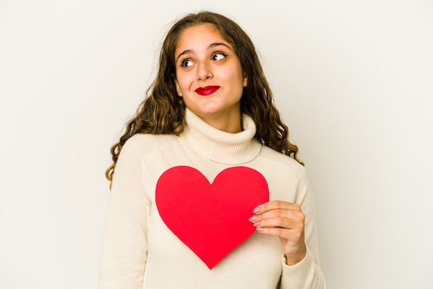 Young caucasian woman holding a heart valentines day shape isolé rêvant d'atteindre les objectifs et buts