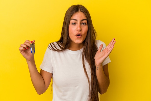 Young caucasian woman holding a home keys isolé sur fond jaune surpris et choqué.