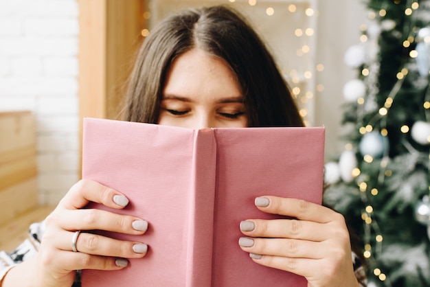 Young Caucasian woman holding livre violet près de l'arbre de Noël décoré