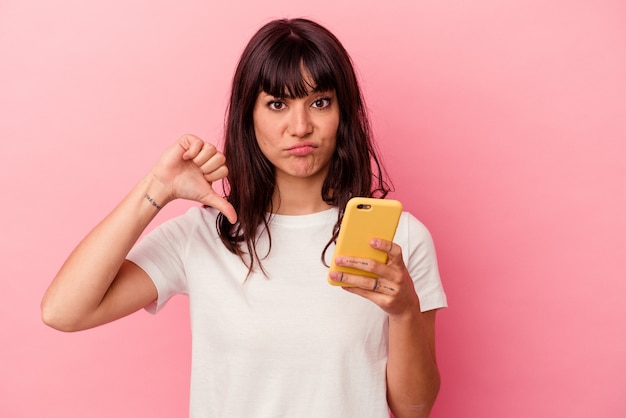 Young caucasian woman holding a mobile phone isolé sur un mur rose montrant un geste de dégoût, les pouces vers le bas