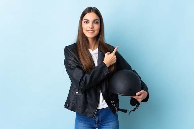 Young caucasian woman holding a moto casque sur bleu pointant vers le côté pour présenter un produit