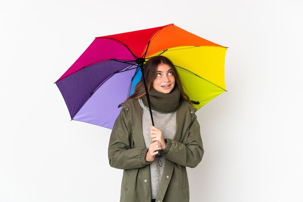 Young caucasian woman holding un parapluie sur blanc pensant une idée tout en levant