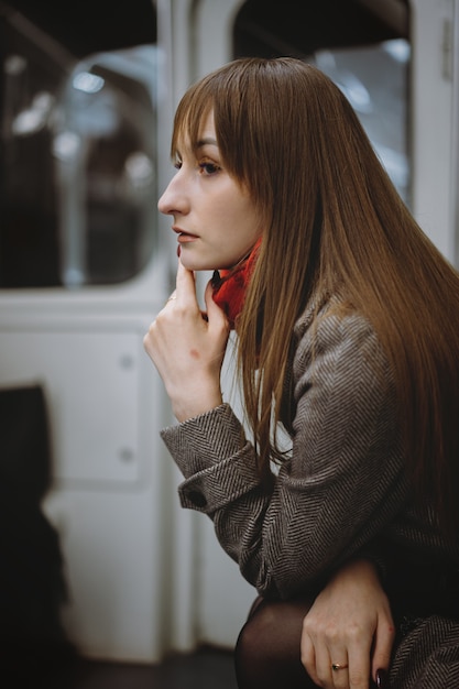 Young caucasian woman in coat assis seul dans une voiture de métro et rêveusement à côté