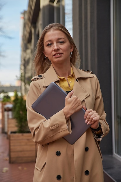 Young caucasian woman in coat holding tablet laptop ou ebook dans les mains à l'extérieur