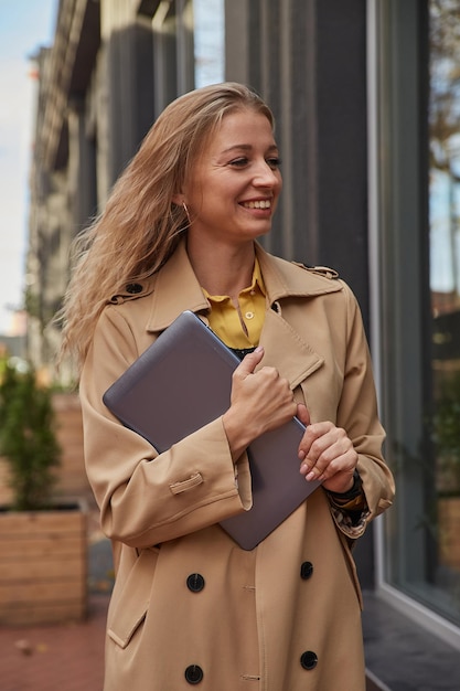 Young caucasian woman in coat holding tablet laptop ou ebook dans les mains à l'extérieur