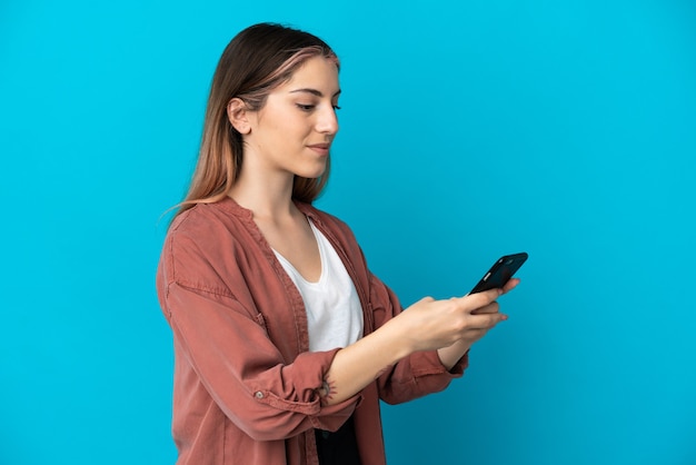 Young caucasian woman isolated on blue envoi d'un message ou d'un e-mail avec le mobile