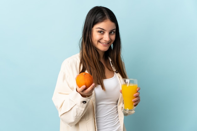 Young caucasian woman isolated on blue tenant une orange et un jus d'orange