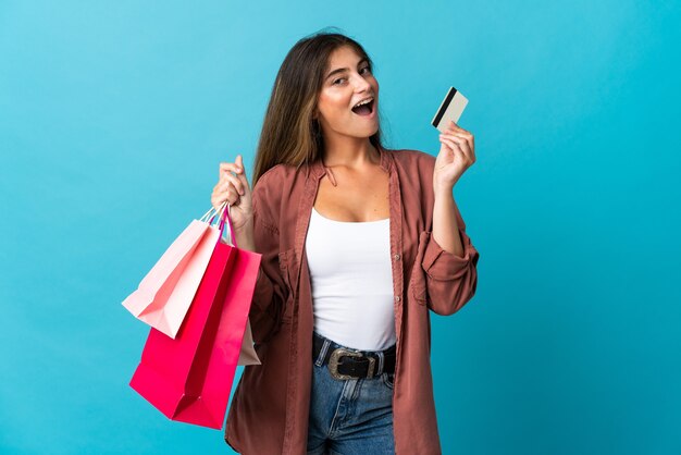 Young caucasian woman isolated on blue wall holding shopping bags et une carte de crédit