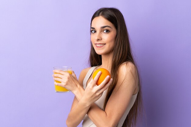 Young caucasian woman isolated on purple tenant une orange et un jus d'orange